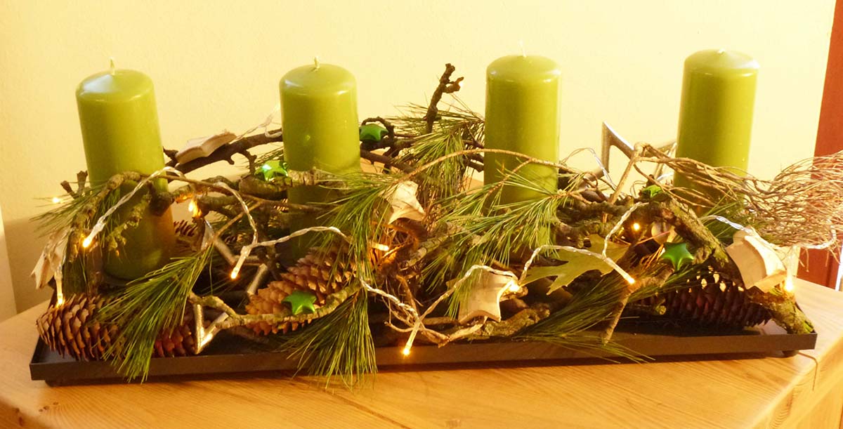 Weihnachtliches Gesteck mit Kerzen und Reißig liebevoll drapiert