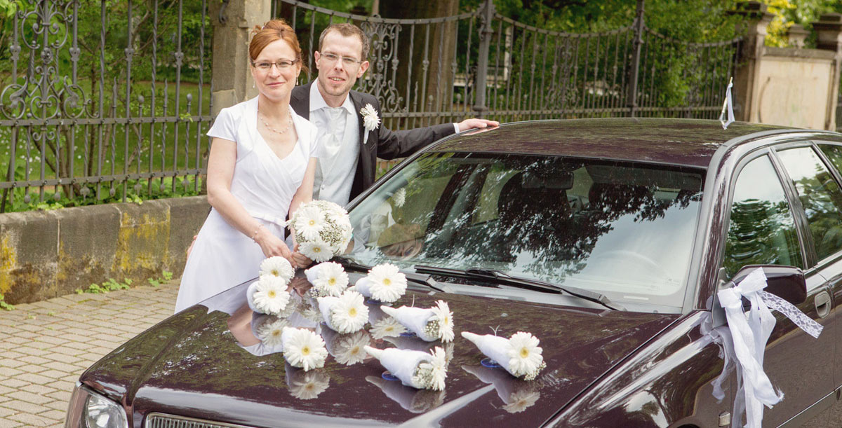 Brautpaar vor ihrem Hcchzeitswagen mit Blumenschmuck