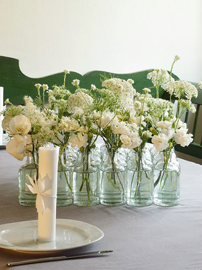 Stilvolle Blumendekoration in kleinen Gläsern verziert mit weißen Frühlingsblühern